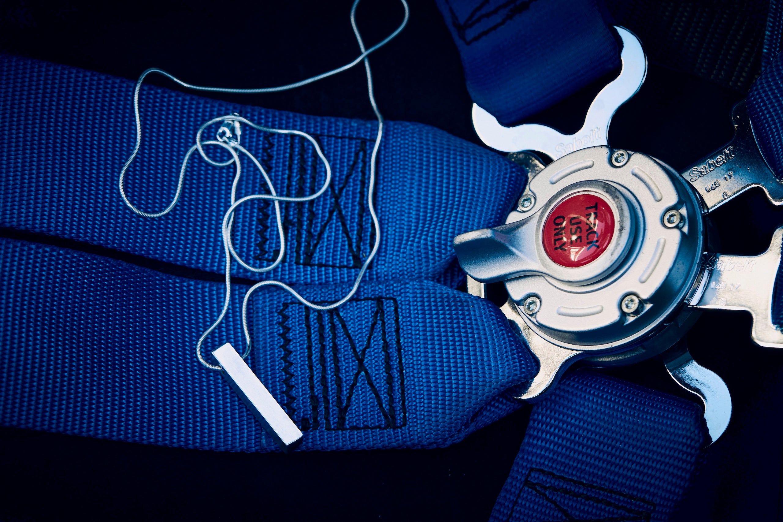 Close-up of a blue race car harness with a RESS jewellery Necklace placed on it.