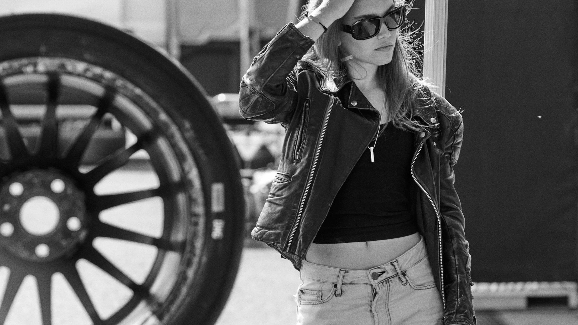 Female model wearing black leather jacket  wearing a RESS necklace made from an F1 car walking down the pit lane at Silverstone circuit in the UK.