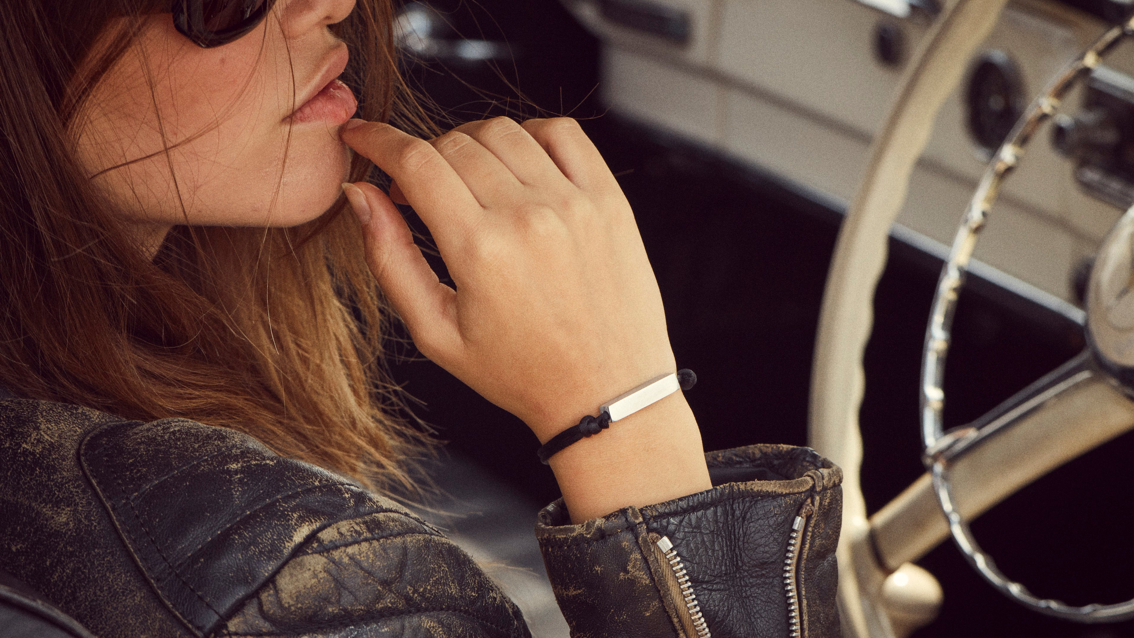 Female model wearing black leather jacket sat in vintage Mercedes road car wearing a RESS bracelet made from an F1 car